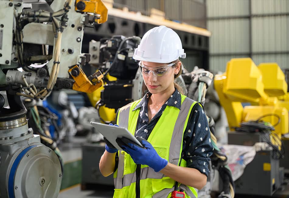 A student wearing a hard hat and reflective vest while examining the machine in a factory.