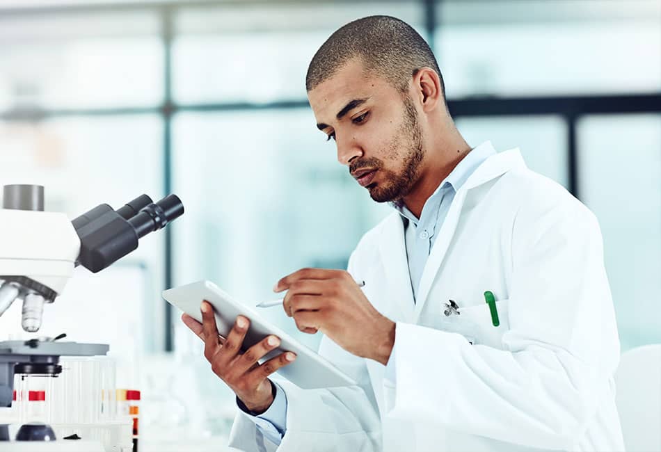 A man in a white coat checking a document in a laboratory with a microscope next to him.