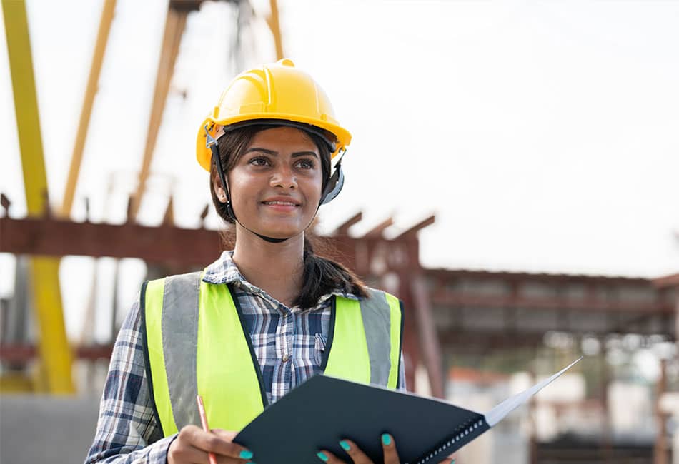 A woman wearing a hard hat and high-visibility vest while examining a construction site.