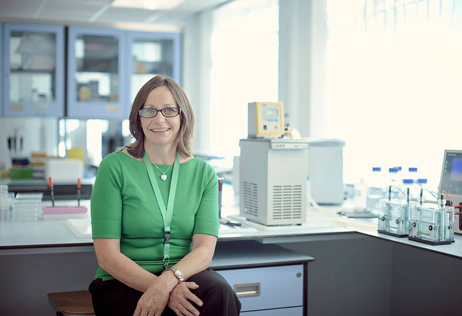 A woman in green blouse sitting on a chair in a laboratory.