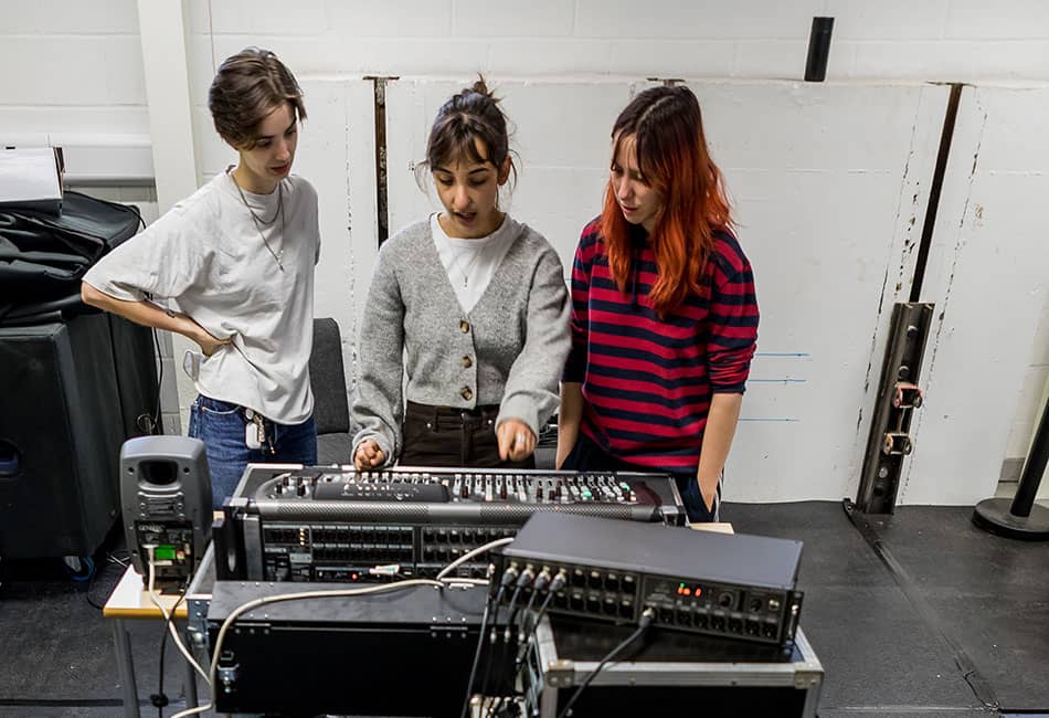 Three students using a mixing desk in a studio.