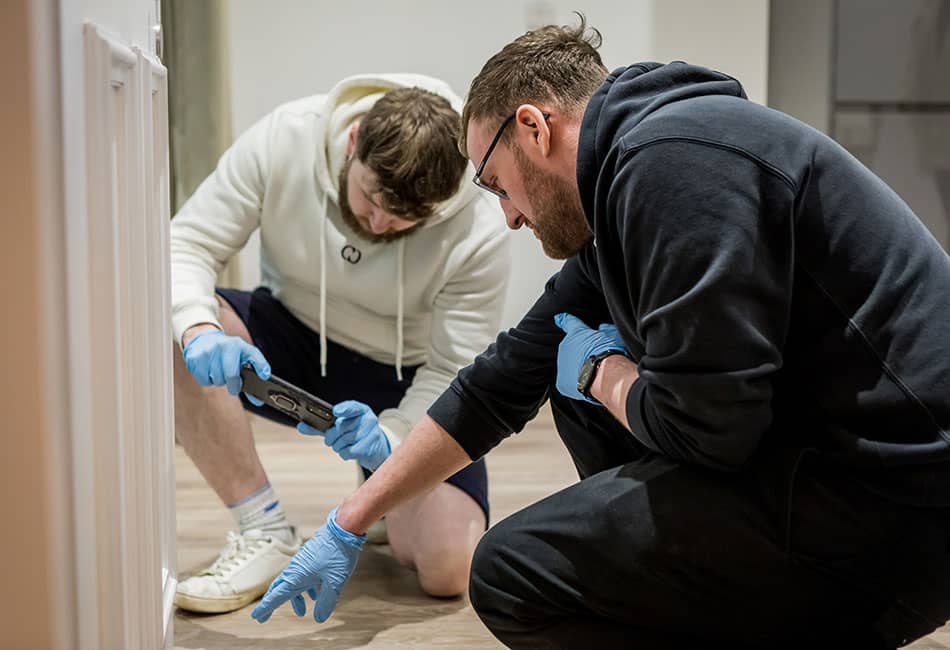 Two people wearing blue nitrile gloves while examining the corner of a house.