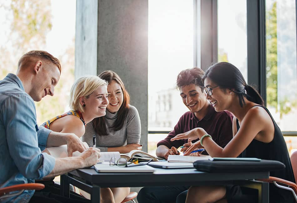 A group of students seated around a table studying and laughing together.